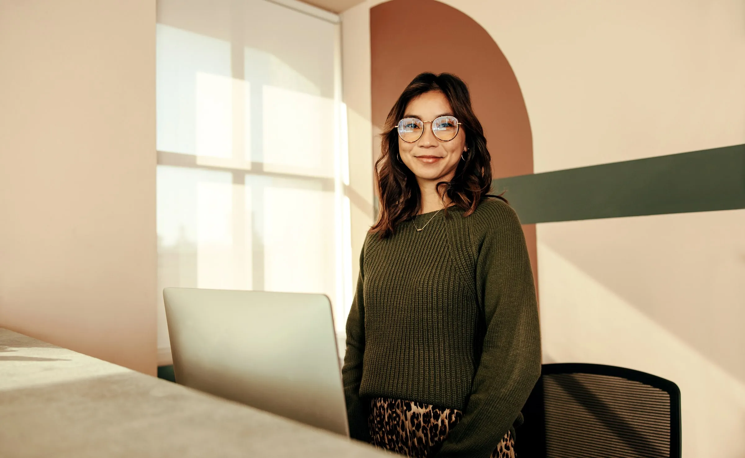 Smiling receptionist in glasses standing behind a front desk in a sunlit office