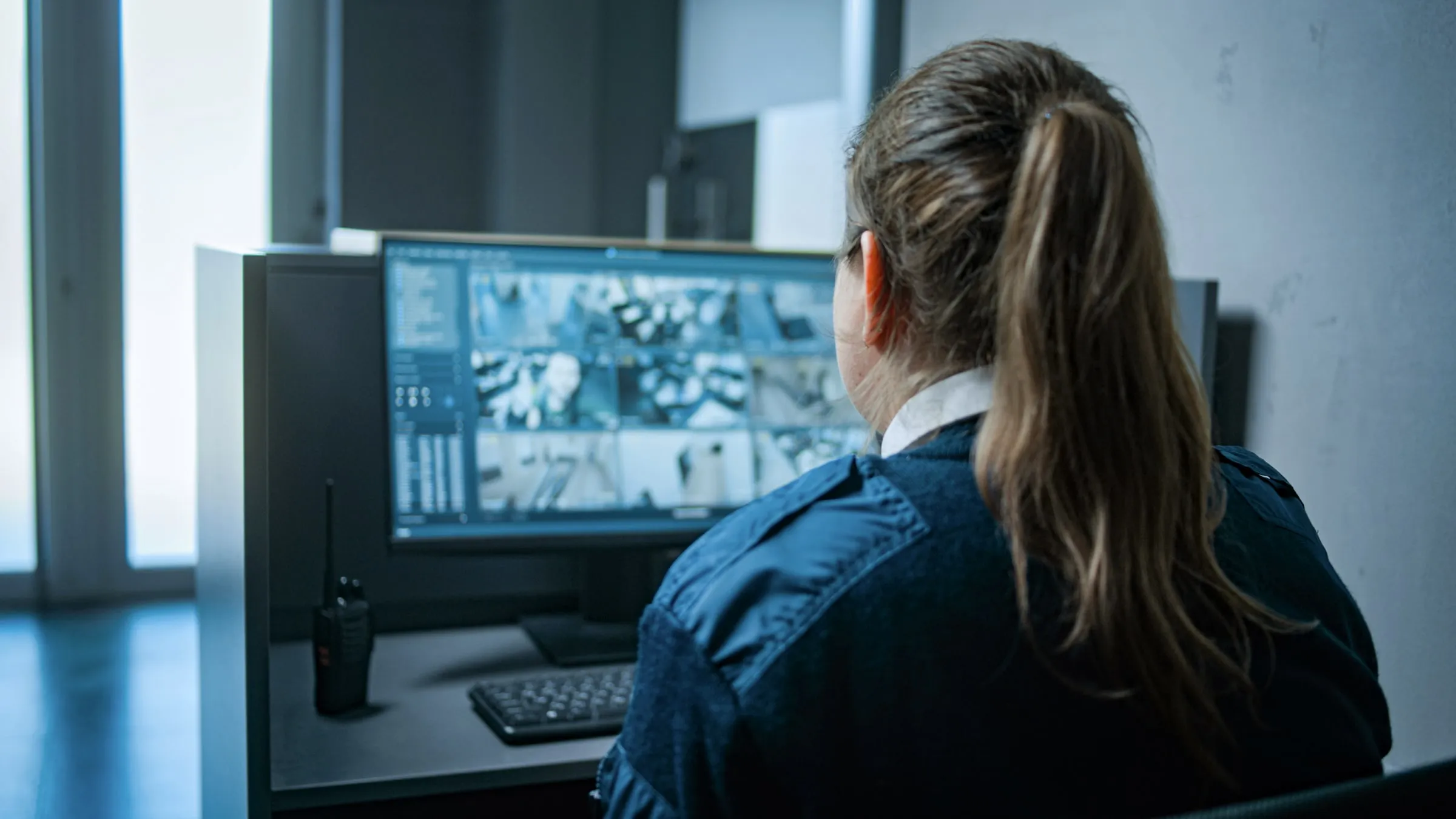 Officer seen from behind at a desk watching a wall of camera monitors
