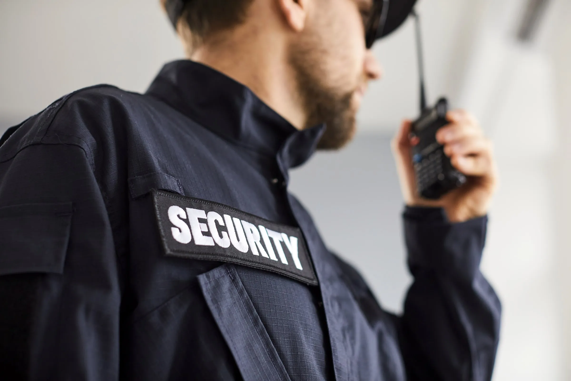Close-up of a security officer's back with a SECURITY patch on a dark uniform, speaking into a handheld radio