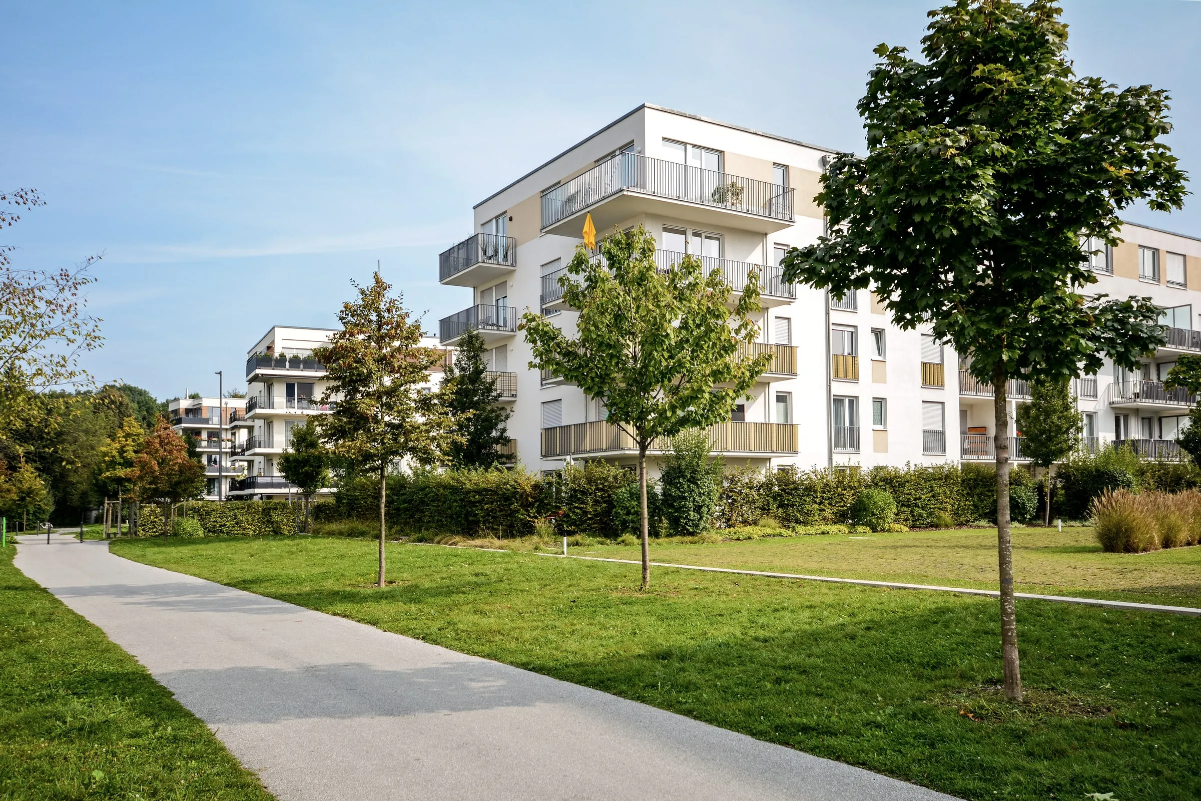 Paved walking path through a landscaped courtyard between white apartment buildings on a clear day