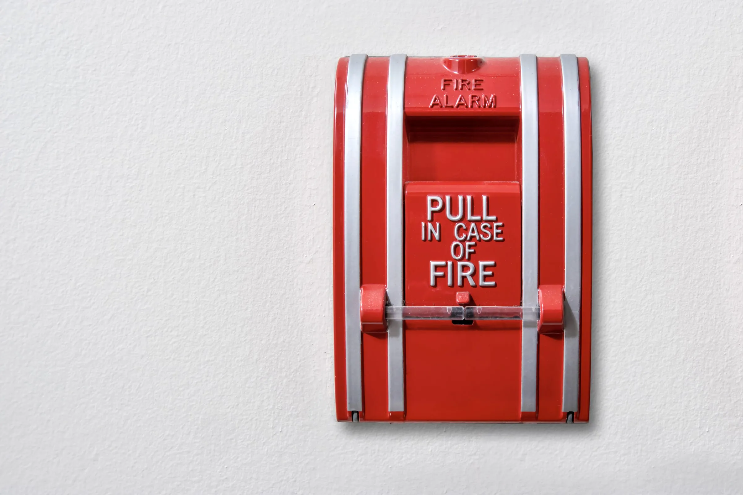 Red fire alarm pull station reading Pull In Case Of Fire mounted on a plain white wall