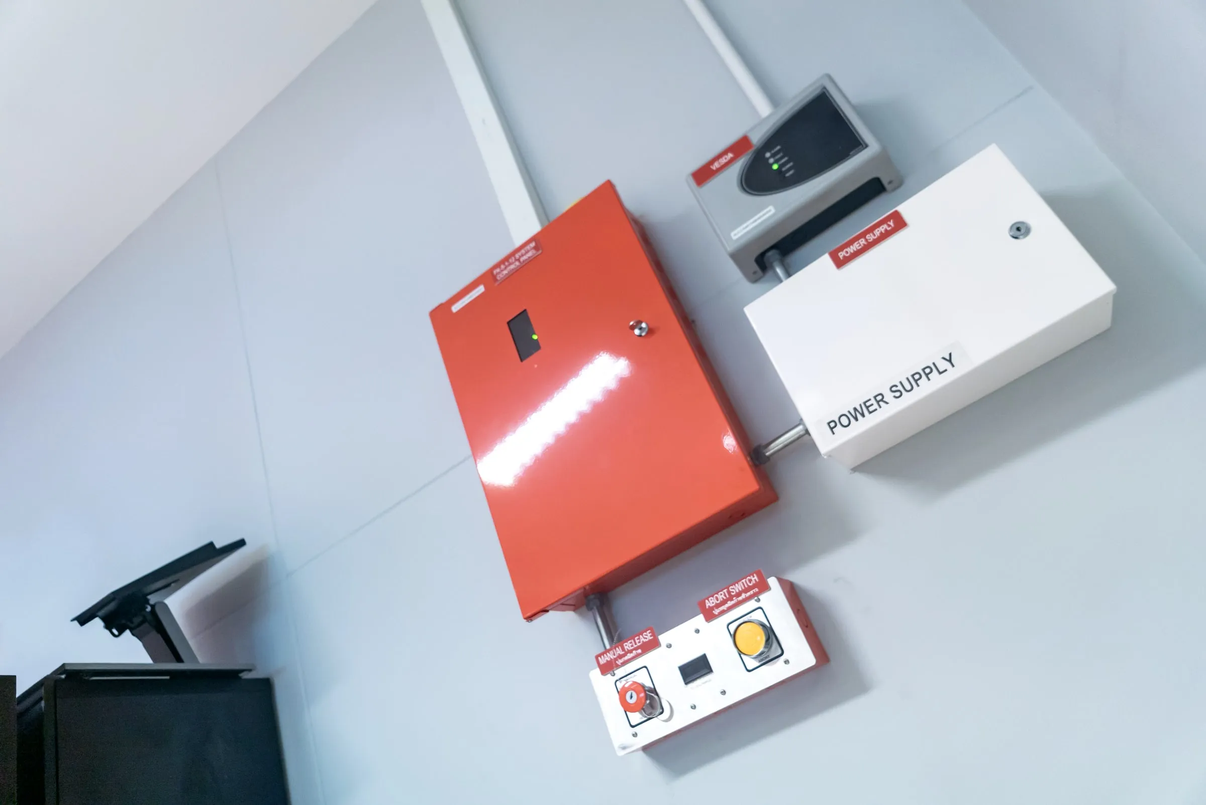 Wall-mounted fire alarm control panel in red and white metal boxes with a manual release key switch and an abort button below