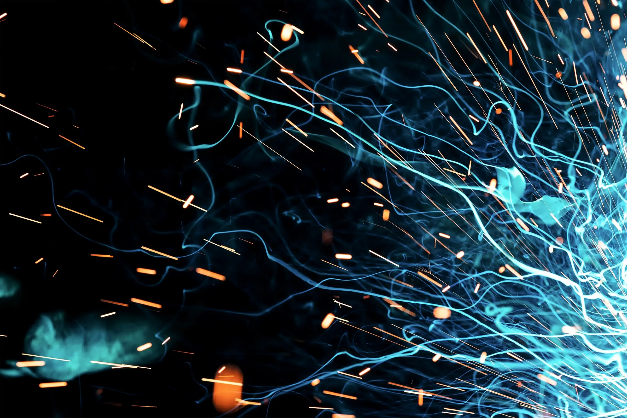 Abstract long-exposure photograph of orange sparks and pale blue light trails streaking across a black background