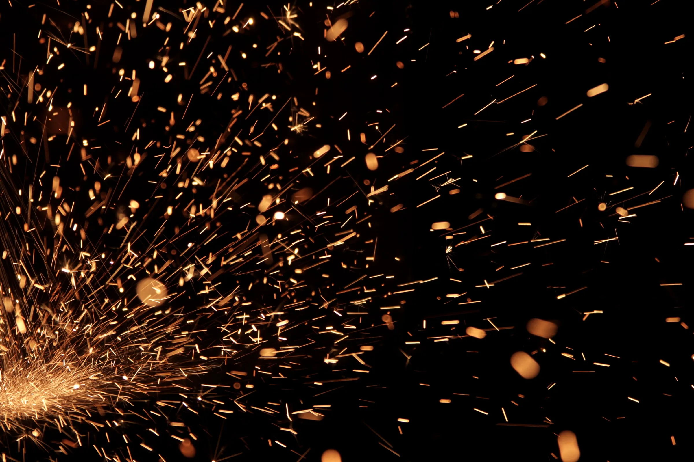 Abstract close-up photograph of bright orange sparks scattering across a black background