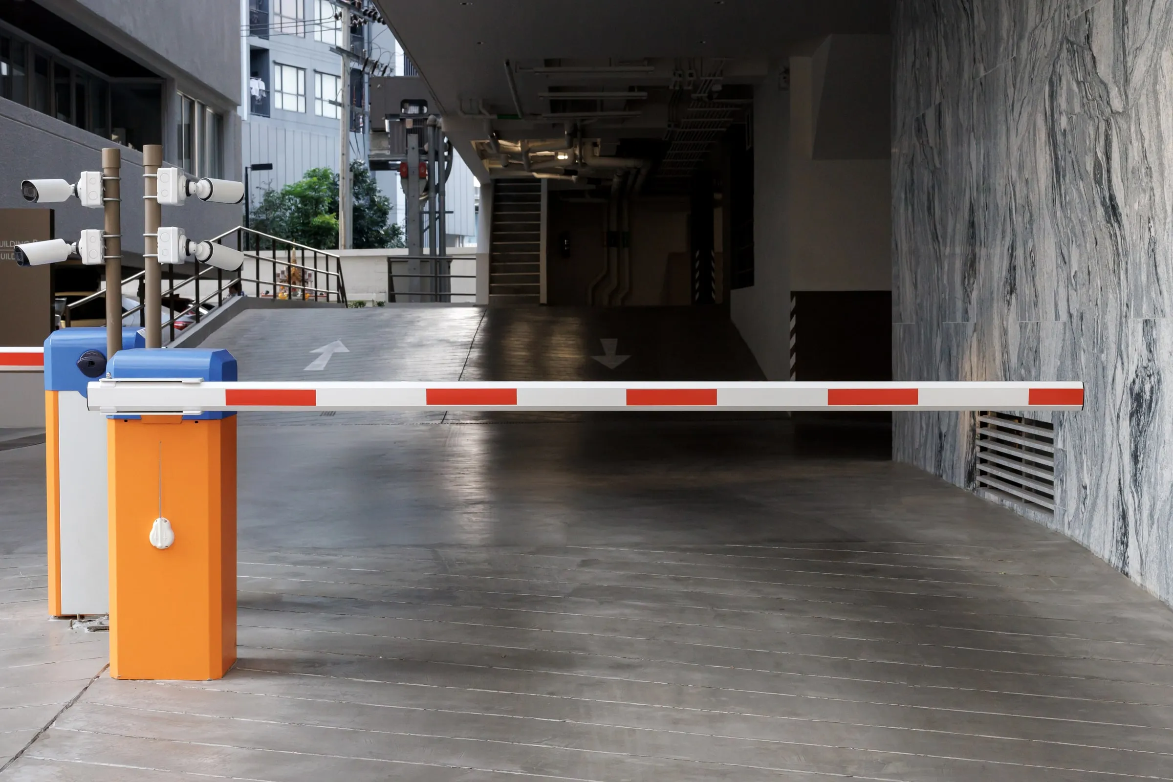 Automated barrier arm gate with red and white stripes beside security cameras on a pole at a parking garage entrance
