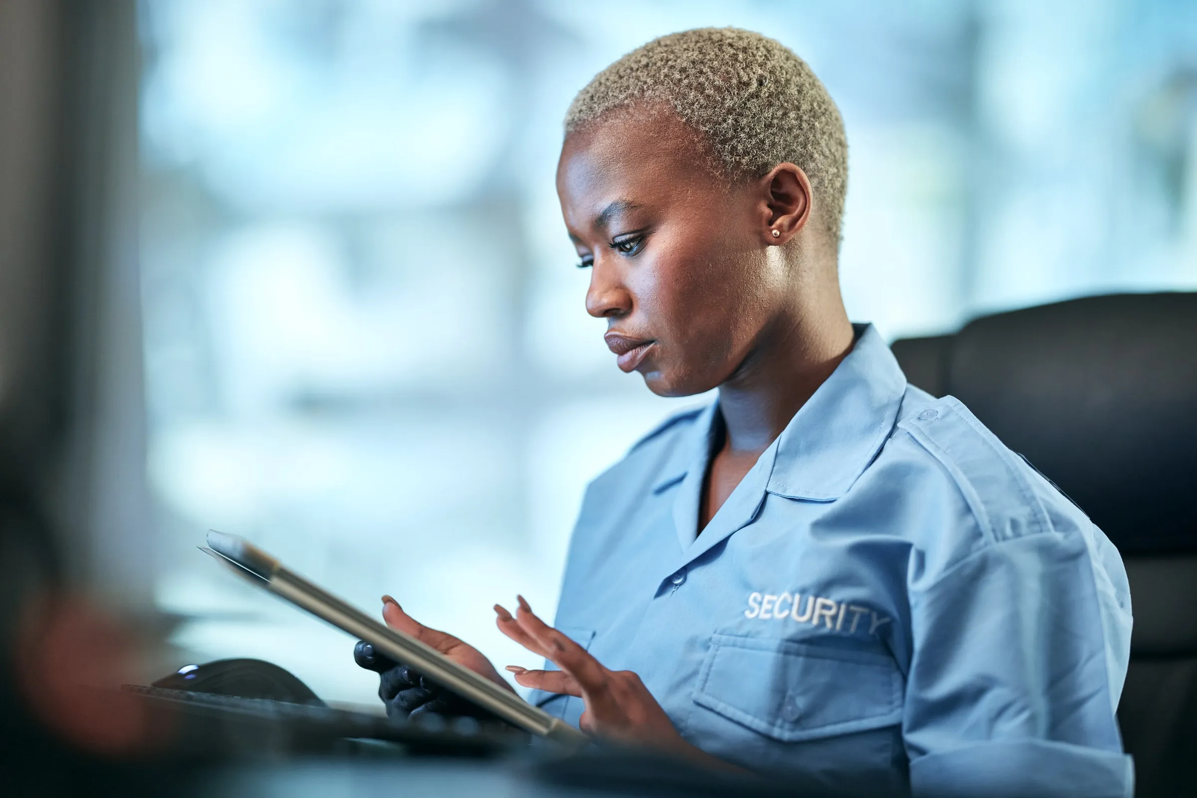 Security officer in a uniform shirt marked SECURITY reviewing information on a tablet indoors