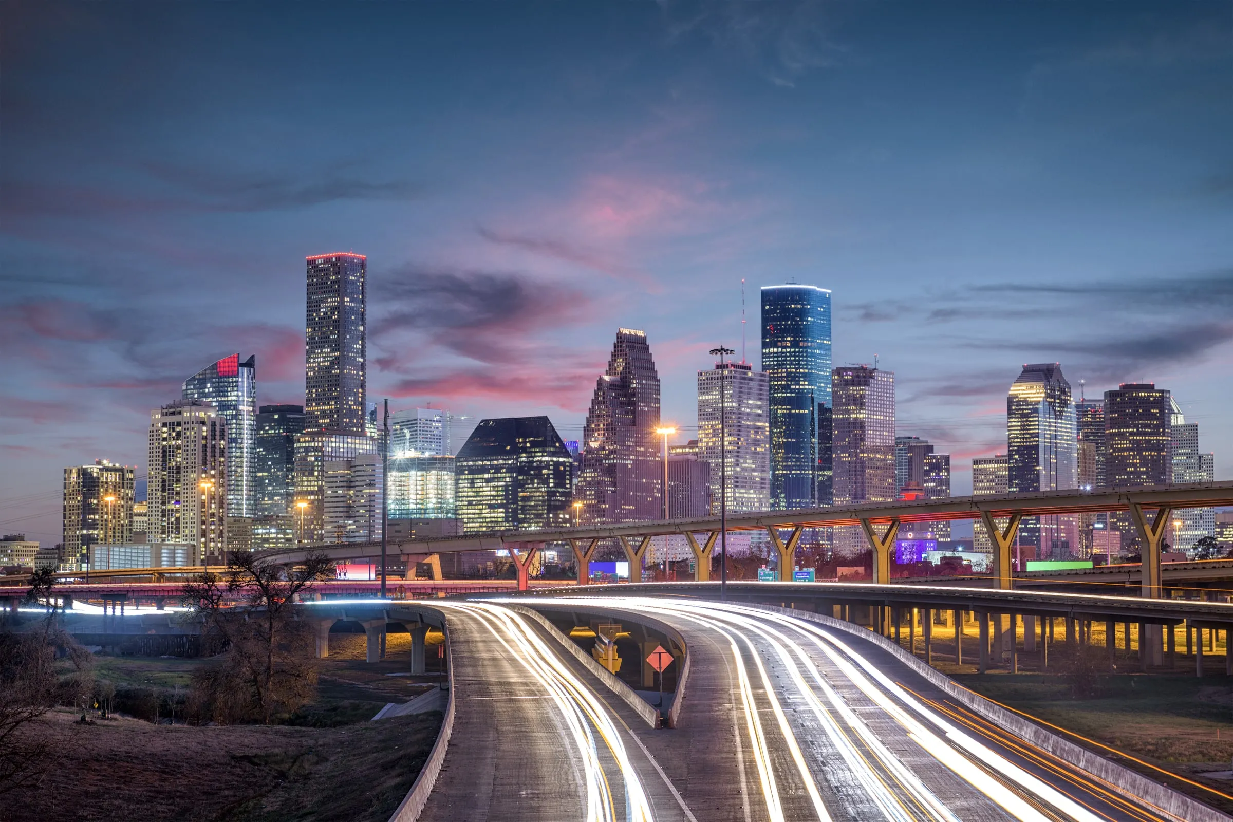 Houston downtown skyline at dusk with light trails from traffic on an elevated freeway interchange
