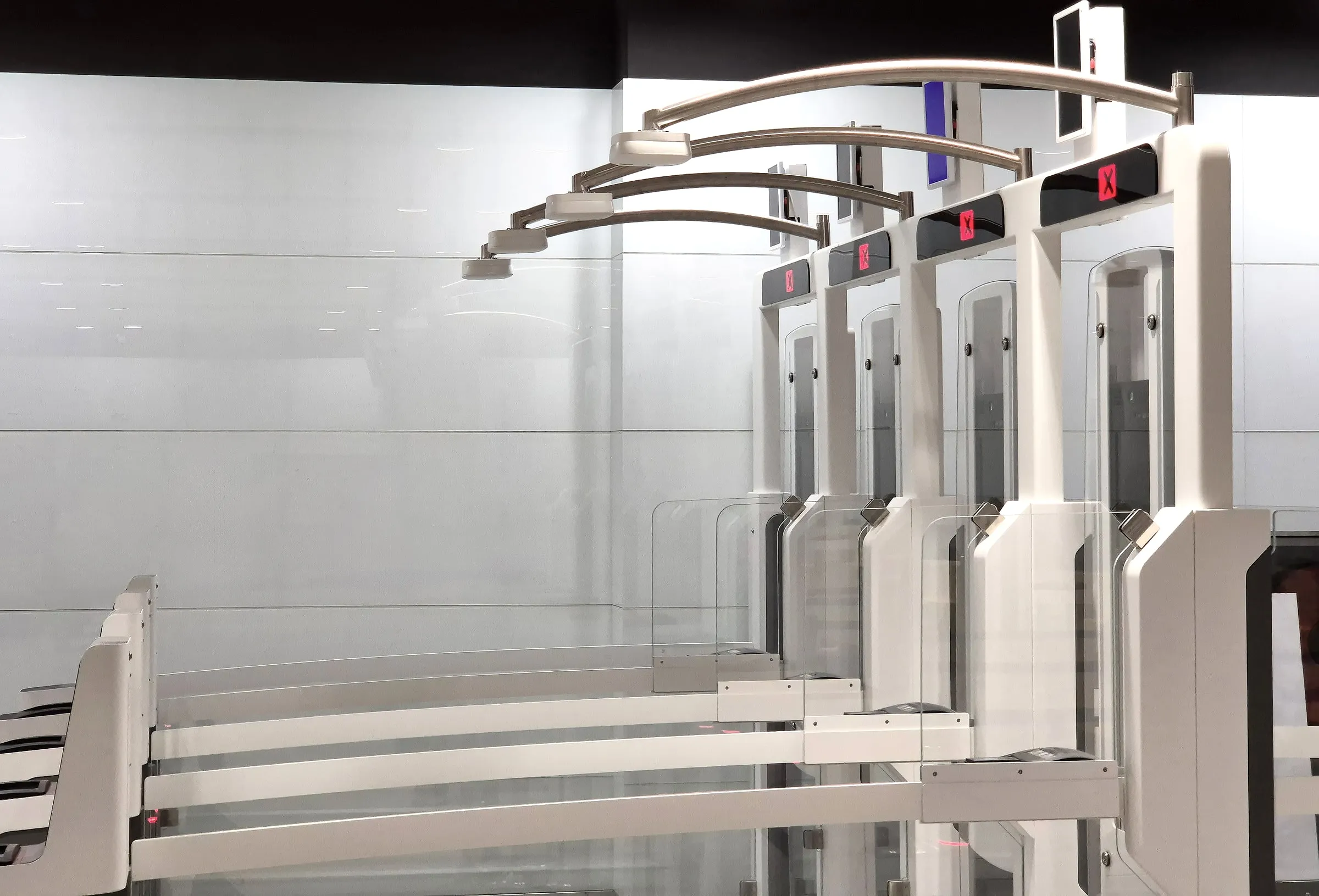 Row of glass turnstile access gates with illuminated red indicator panels in a modern lobby
