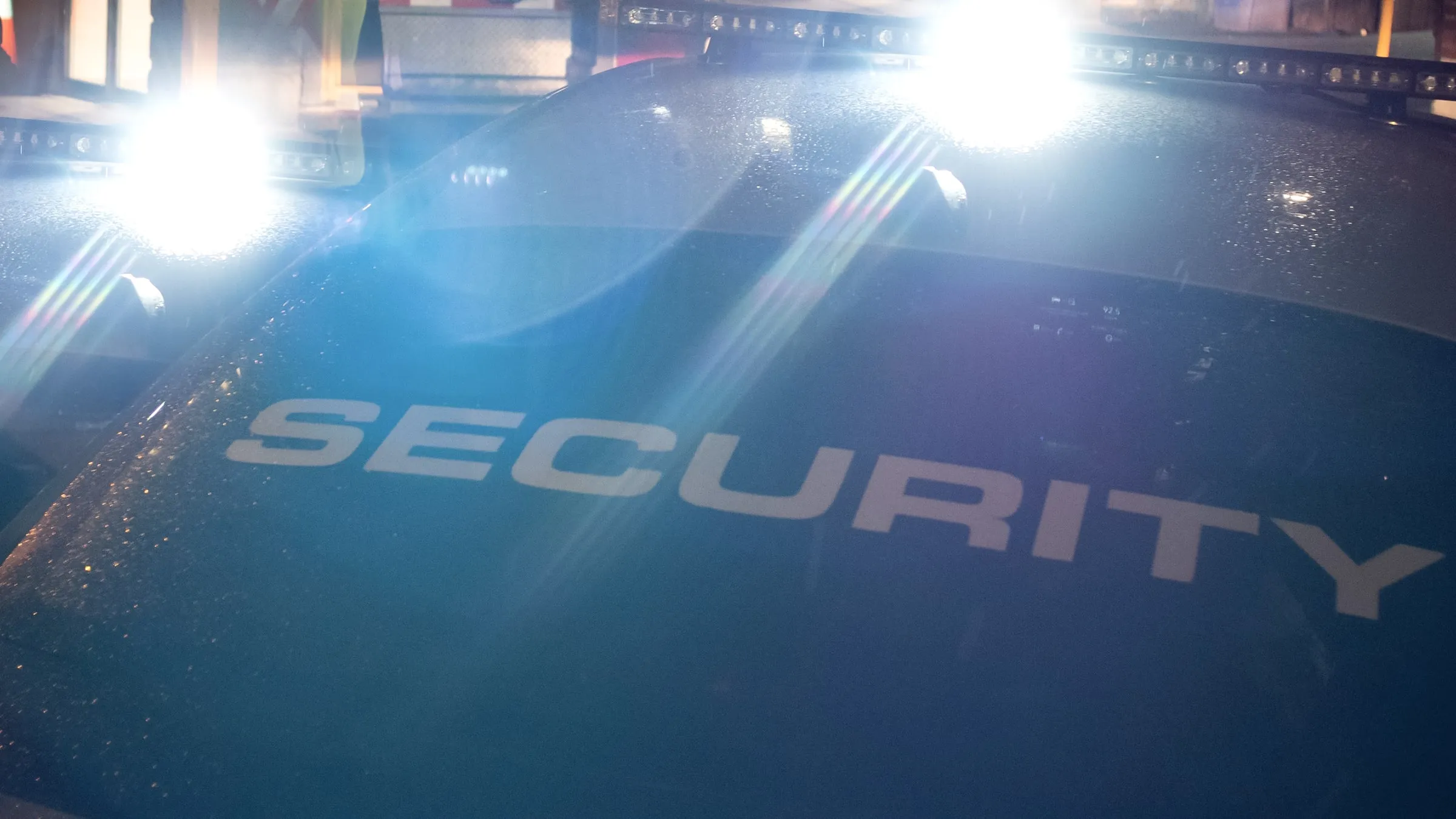 Close-up of a dark patrol vehicle's roof at night with SECURITY lettering, lit by the glare of its own light bar