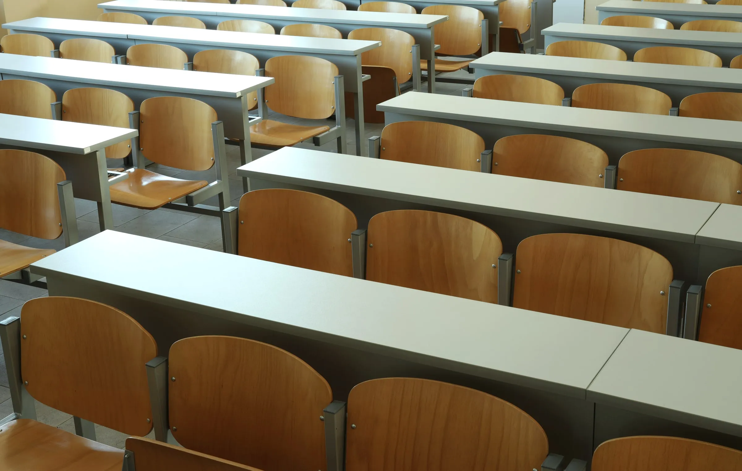 Rows of empty wooden desks with attached chairs in a daylit training classroom