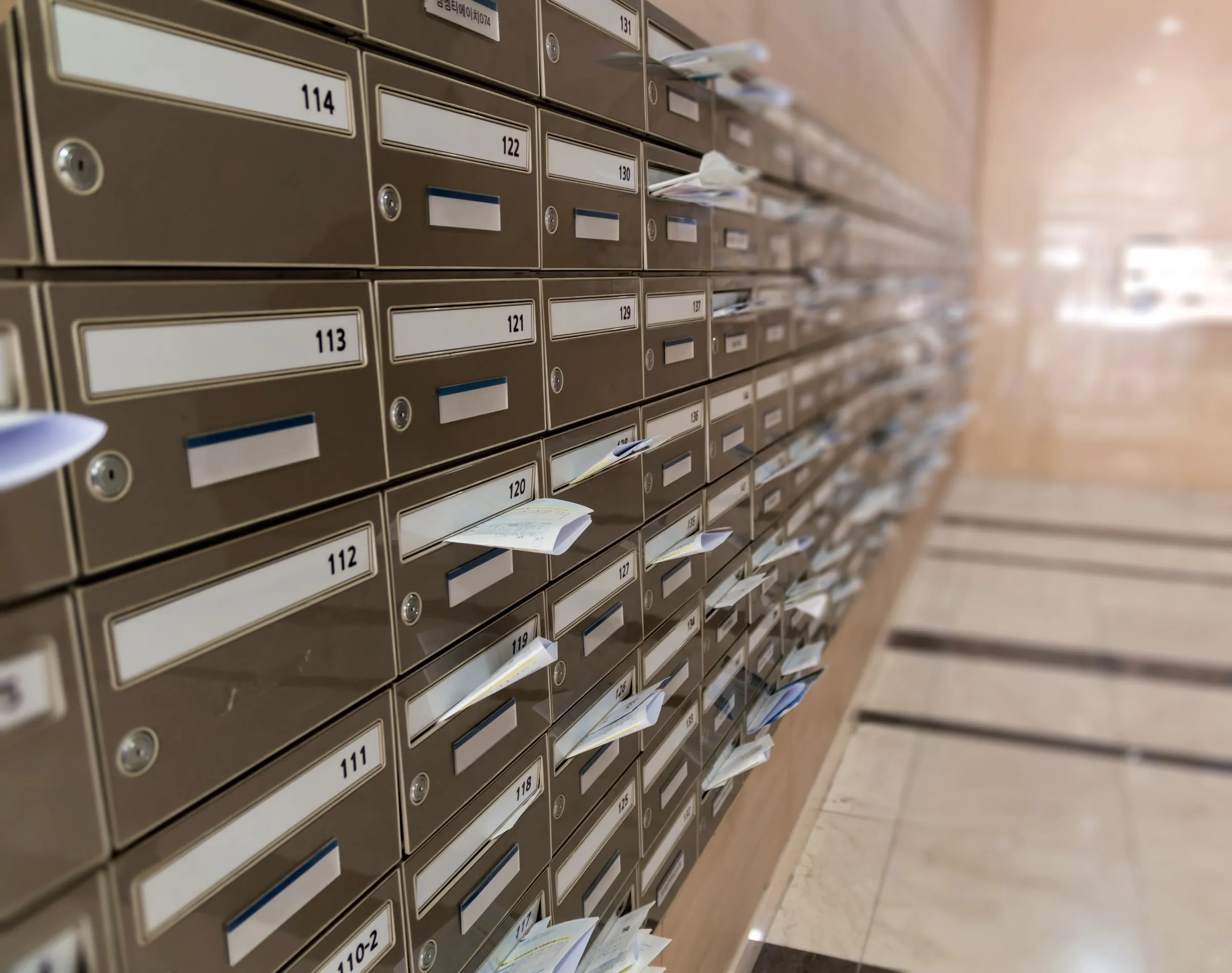 Wall of numbered apartment mailboxes with mail and envelopes protruding from several open slots
