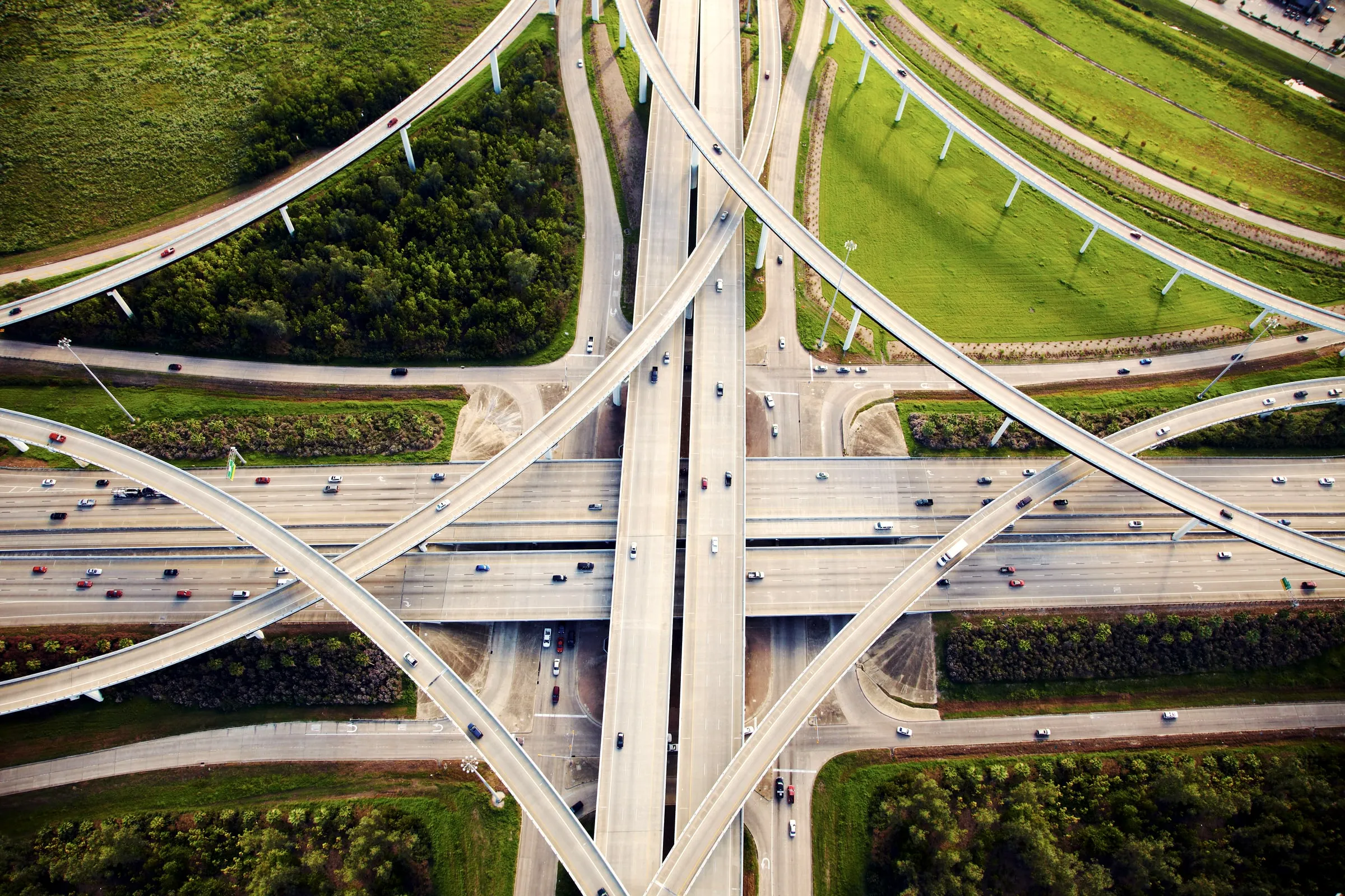 Aerial view of a multi-level highway interchange with light traffic, surrounded by green fields