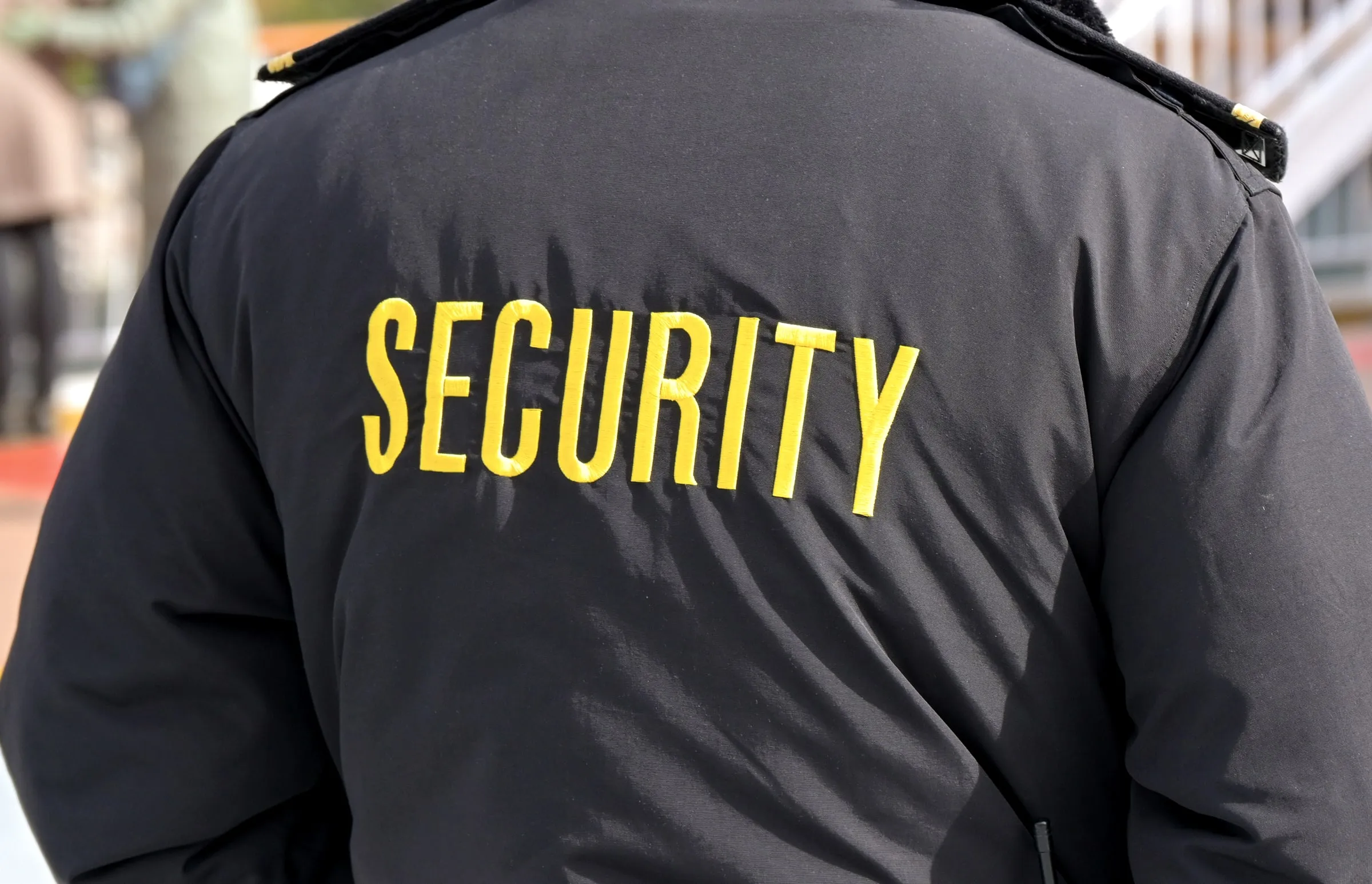 Back of a security officer's dark jacket embroidered with SECURITY in yellow lettering