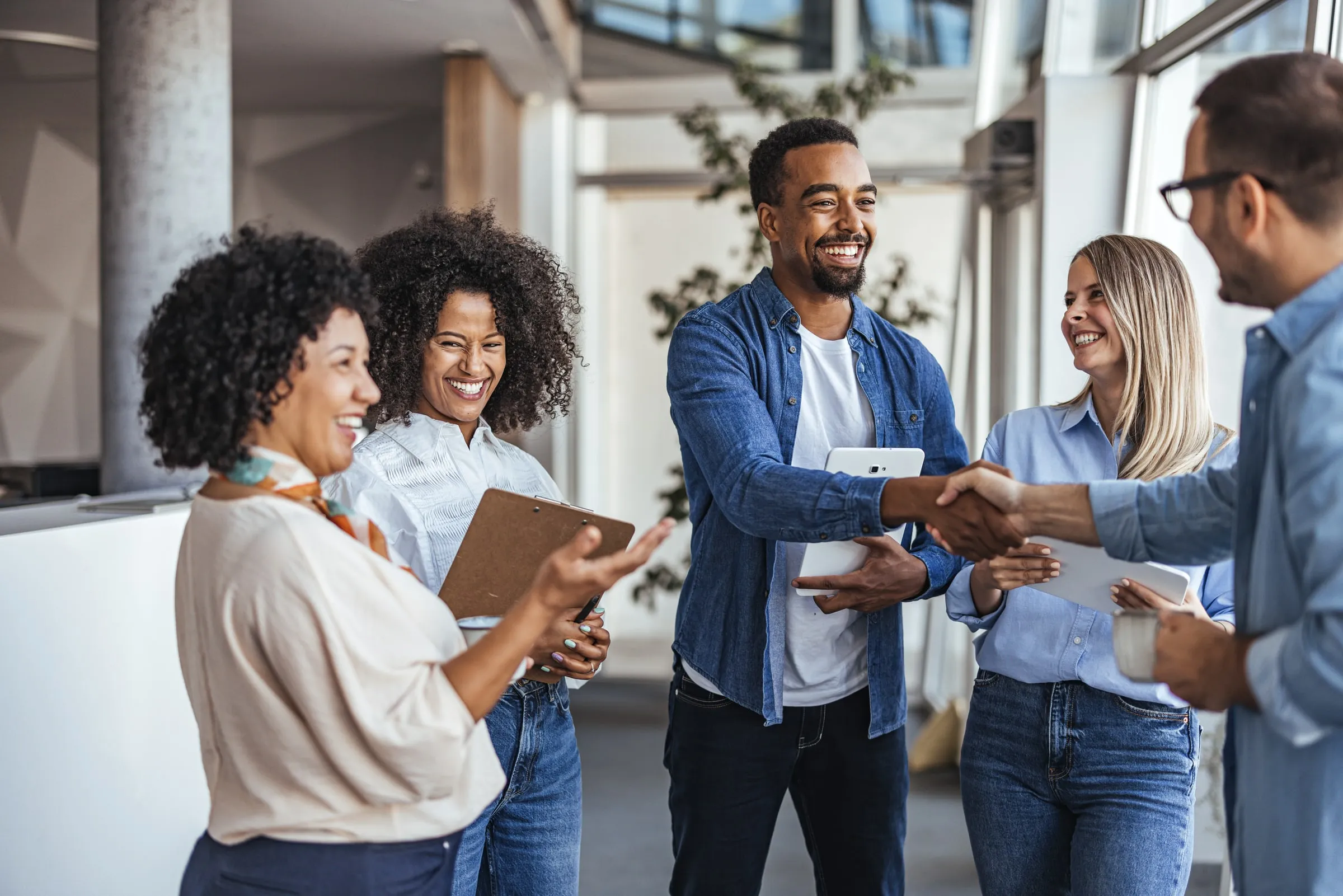 Group of coworkers smiling and shaking hands in a bright office lobby during an introduction