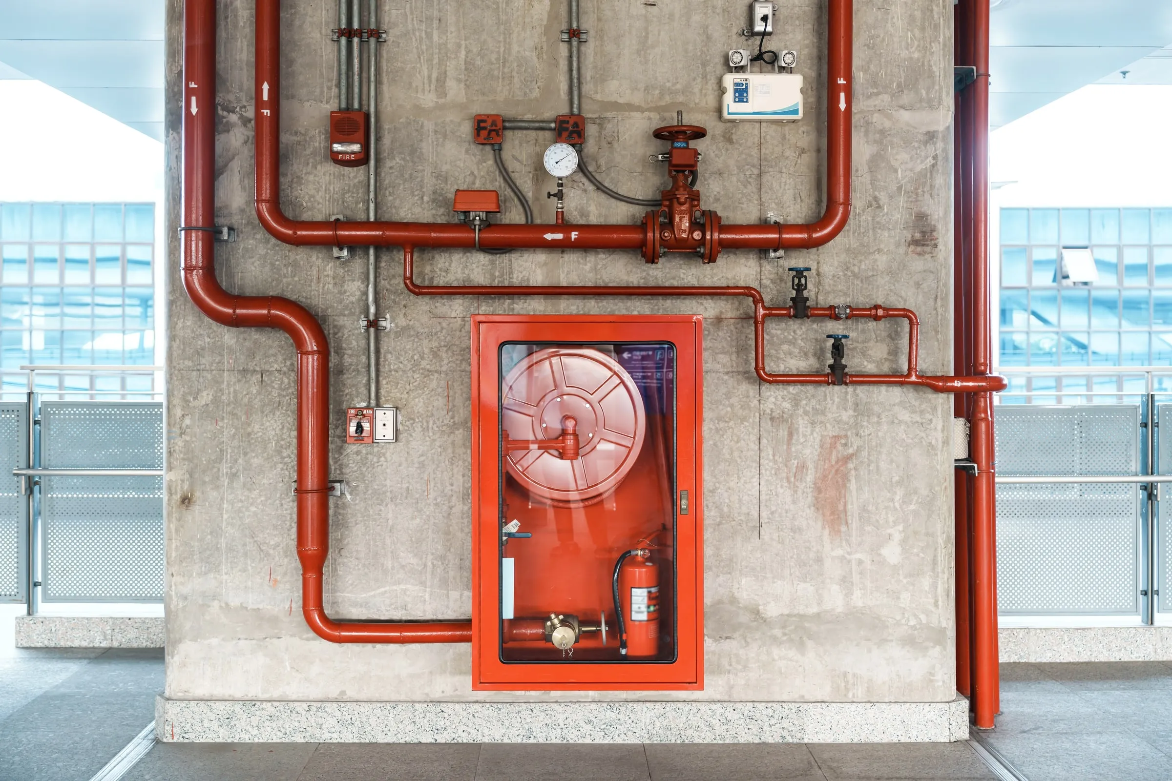 Standpipe cabinet with a hose reel, valves, gauges and a fire alarm pull station mounted on a concrete wall
