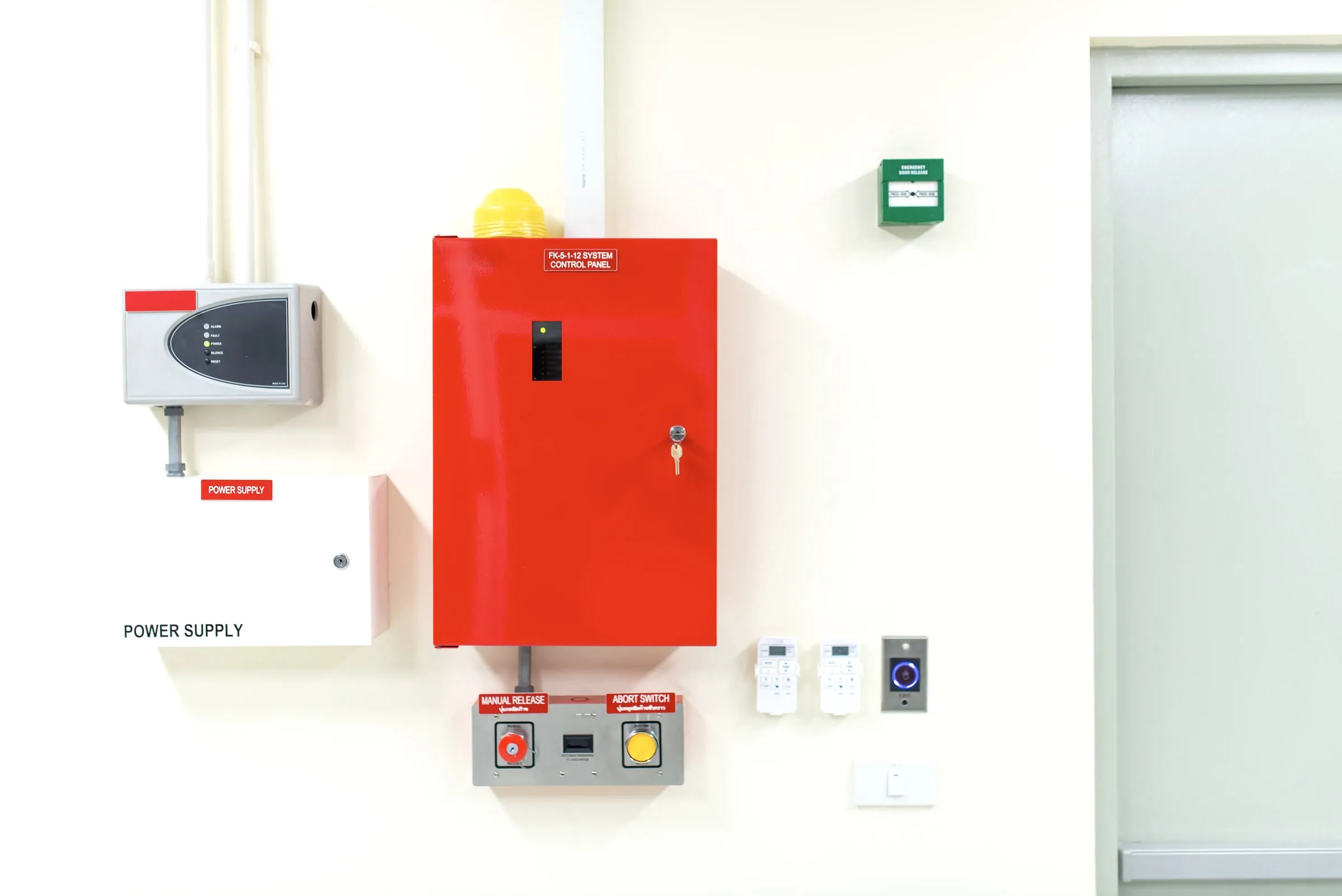 Red FK-5-1-12 system control panel with manual release and abort switch buttons mounted on a wall beside a power supply box