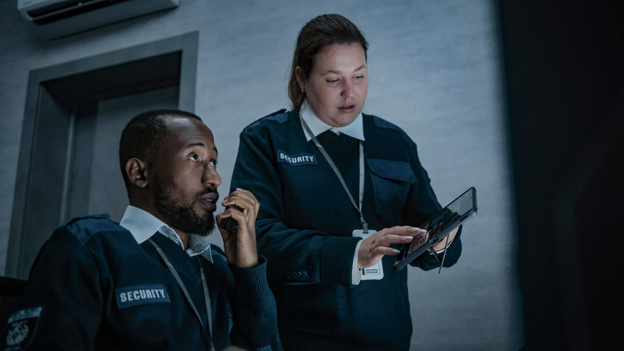 Two security officers, one on a radio and one logging notes on a tablet