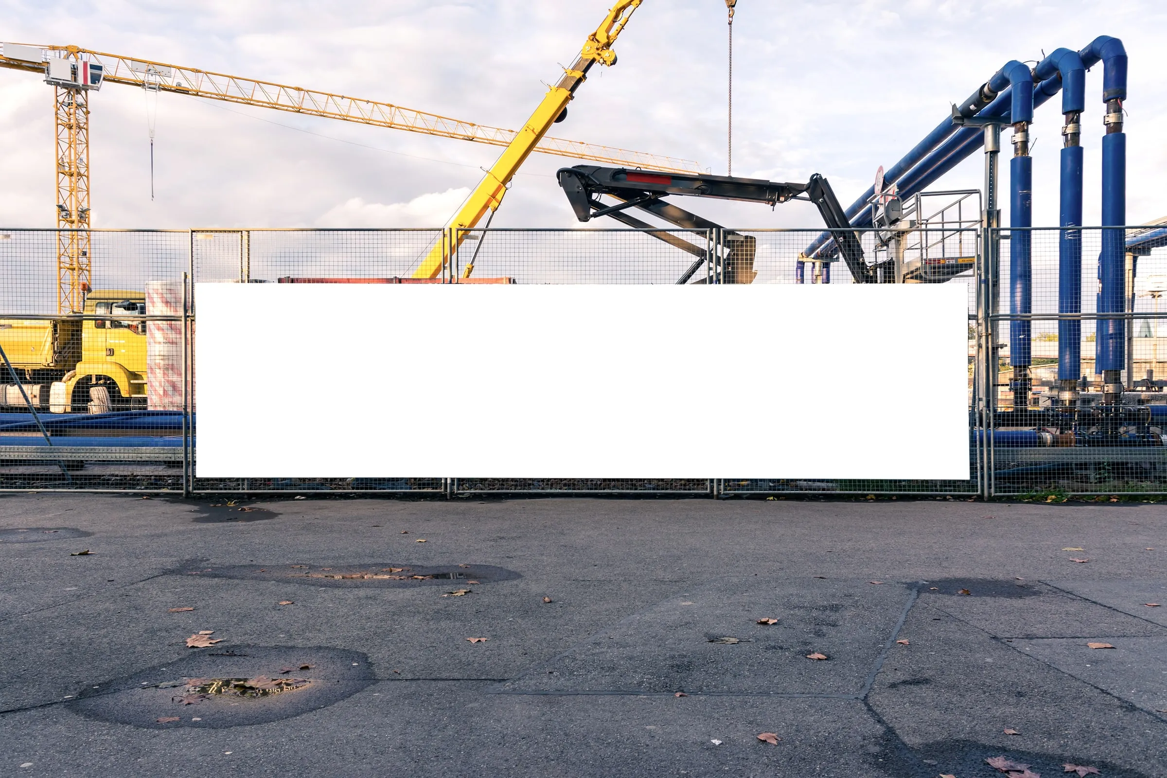 Blank white sign board on a fence in front of cranes and a construction site under a cloudy sky