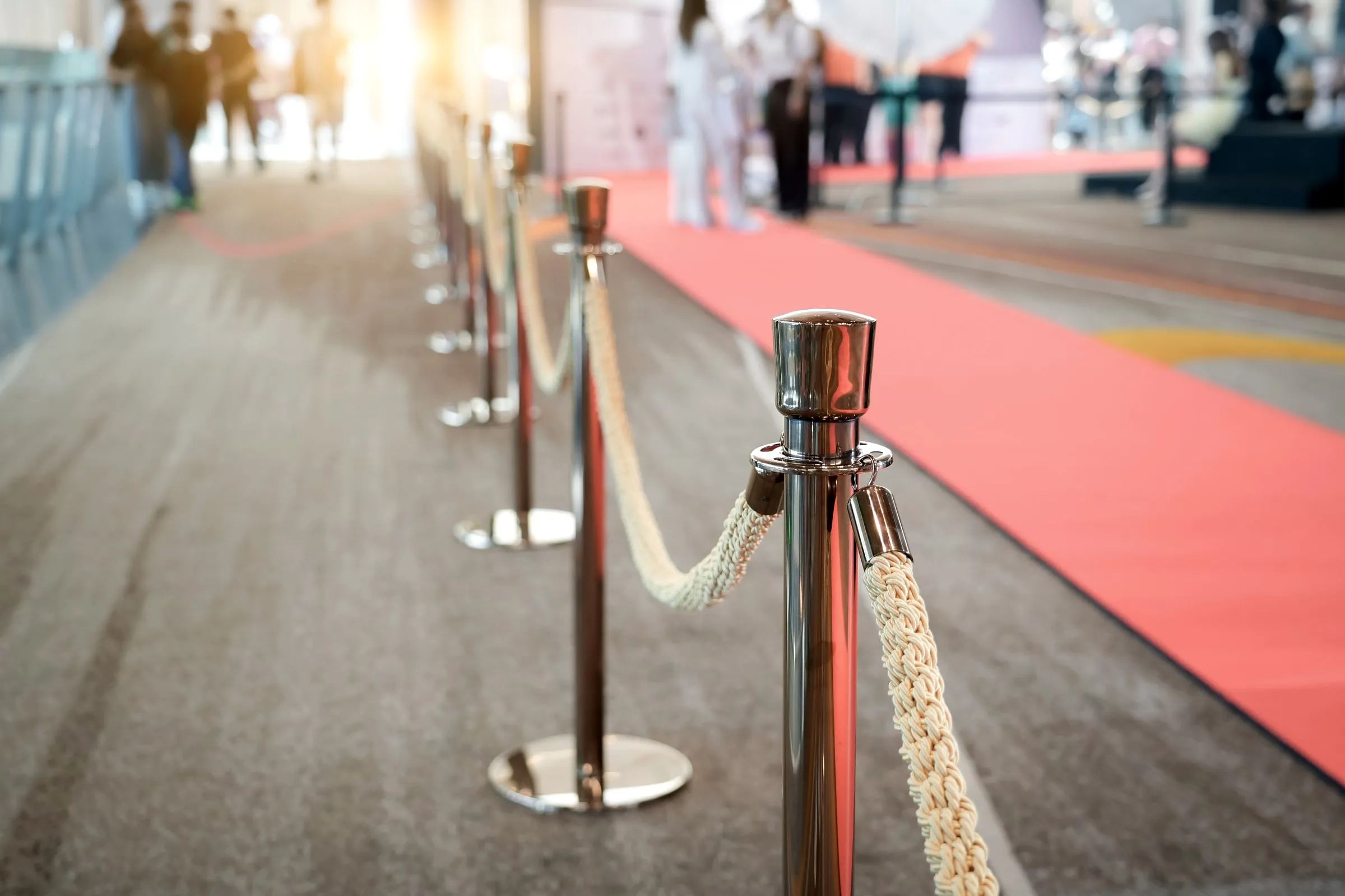 Red carpet lined with chrome stanchions and rope leading toward an event entrance