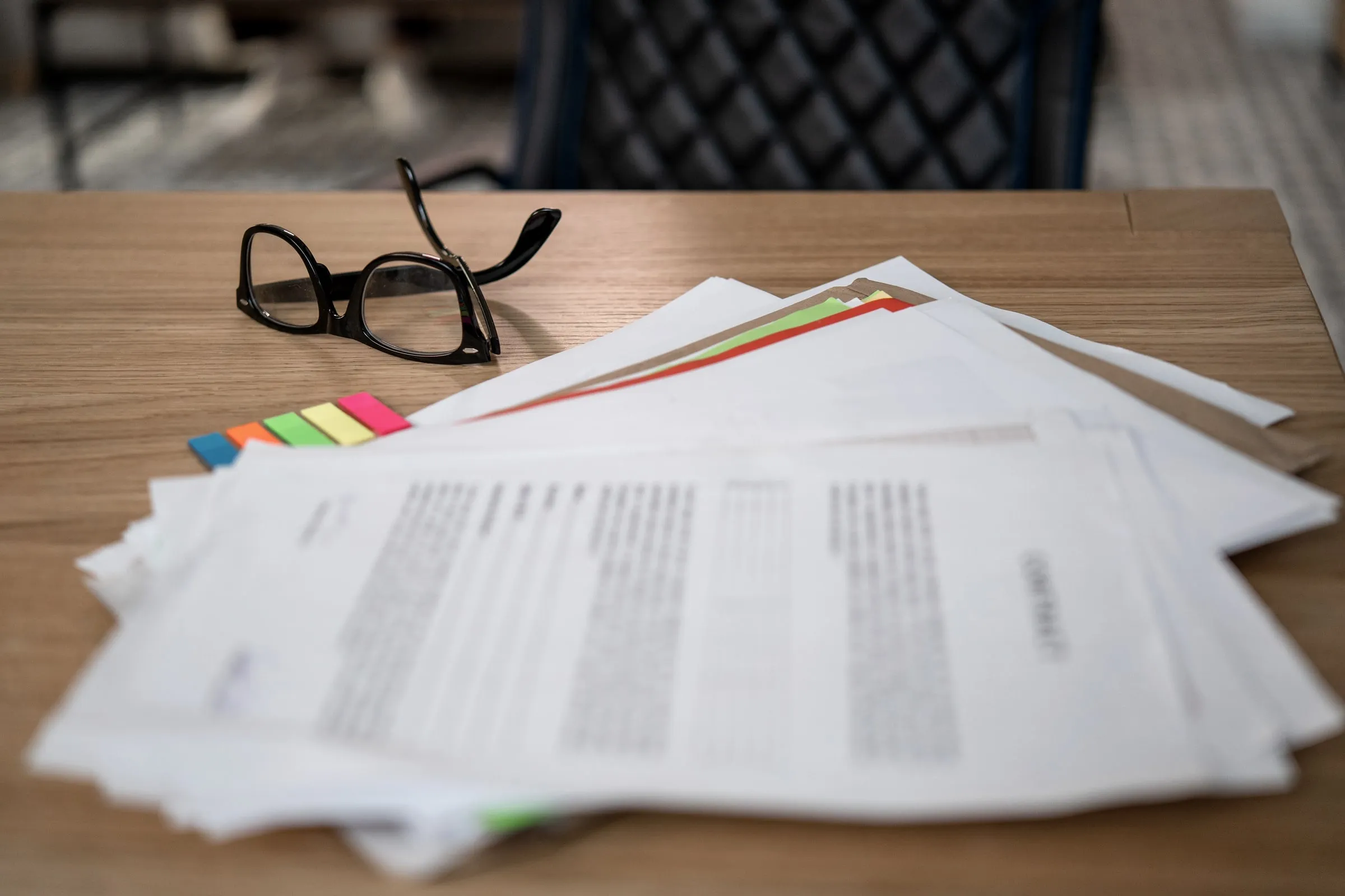 Stack of printed proposal pages with colored tabs and a pair of glasses on a desk