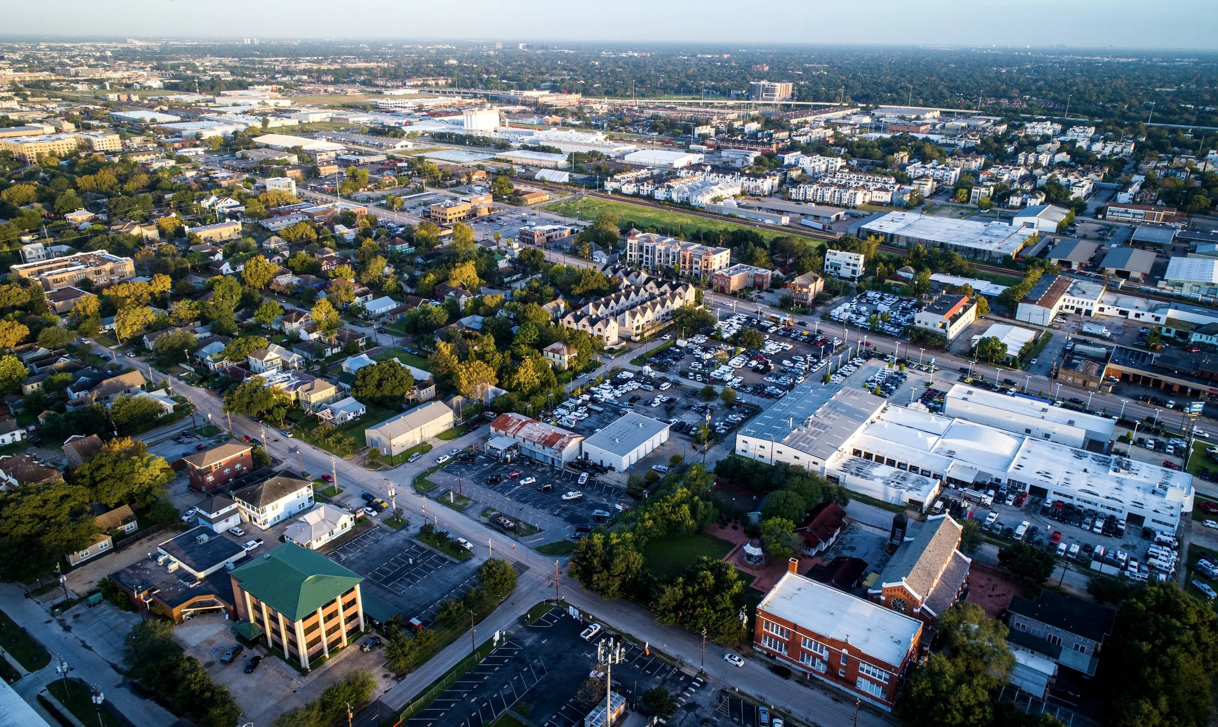 Aerial view of a leafy neighborhood of single-family homes with a commercial strip and office buildings on the horizon