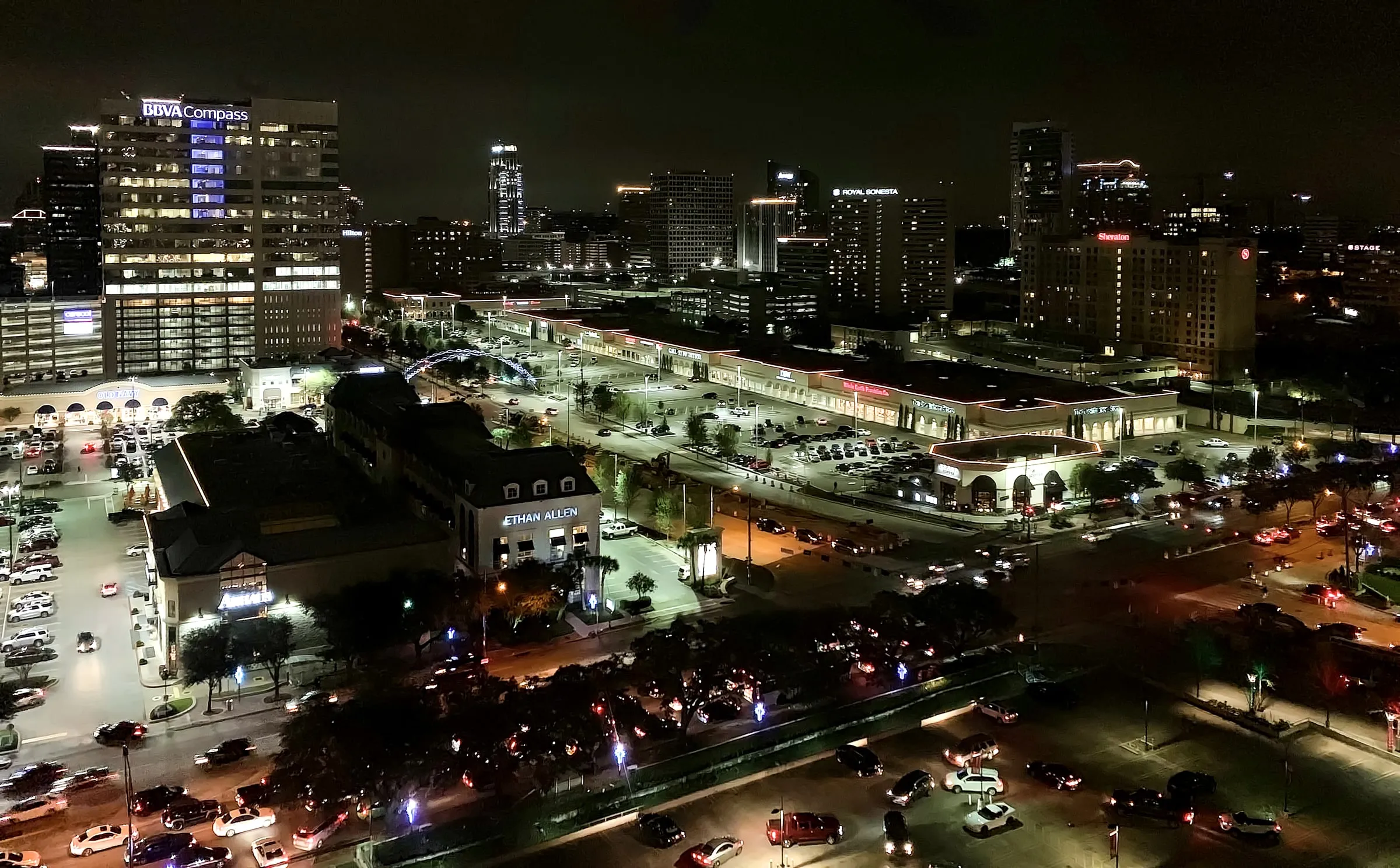 Aerial view of Houston's Uptown district at night, with lit towers, the freeway and a landscaped park