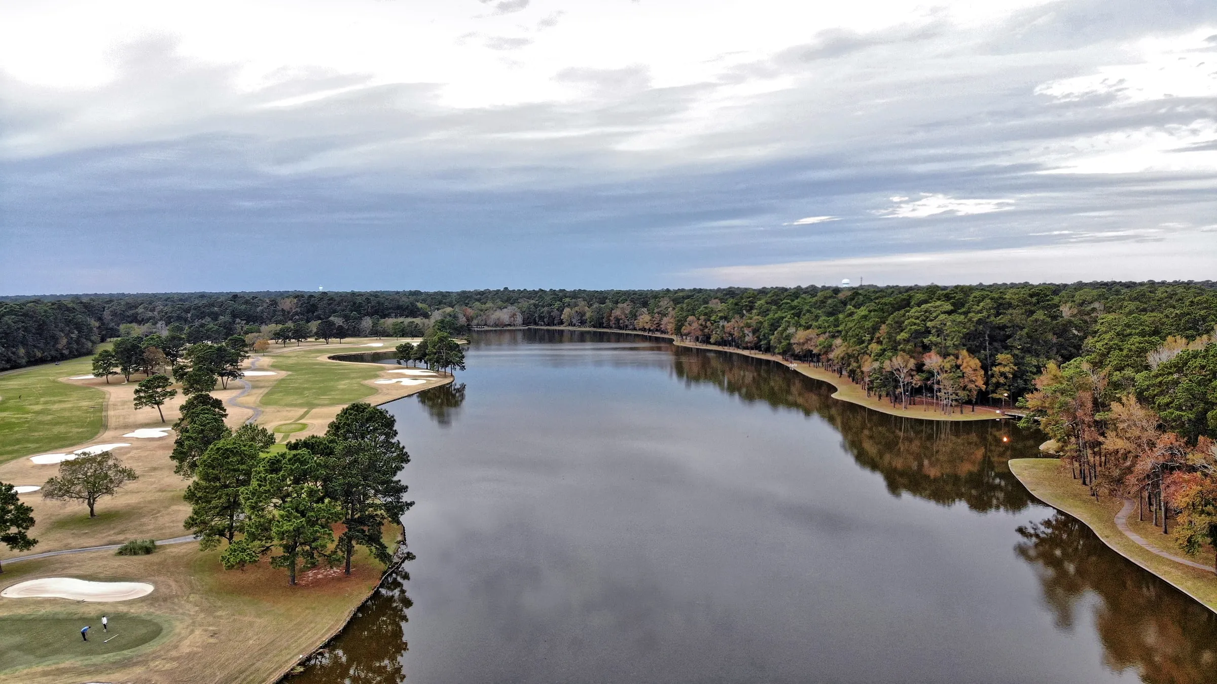 Aerial view of a calm lake bordered by dense pine forest with a walking path along the shore