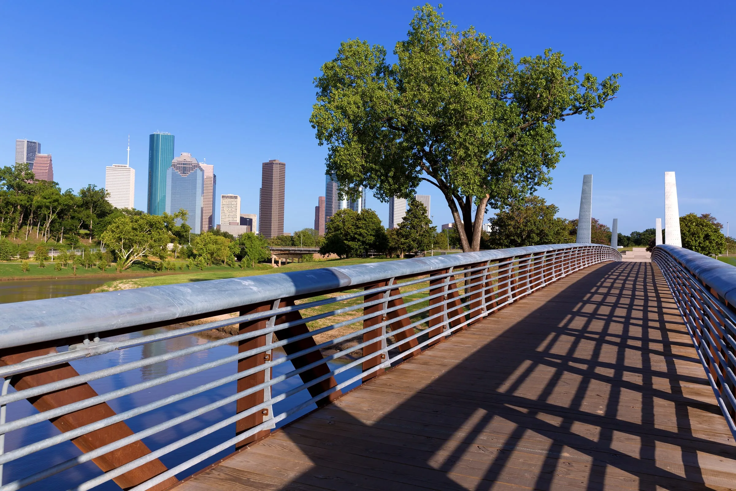 Pedestrian bridge with steel cables leading toward the Houston skyline on a clear day