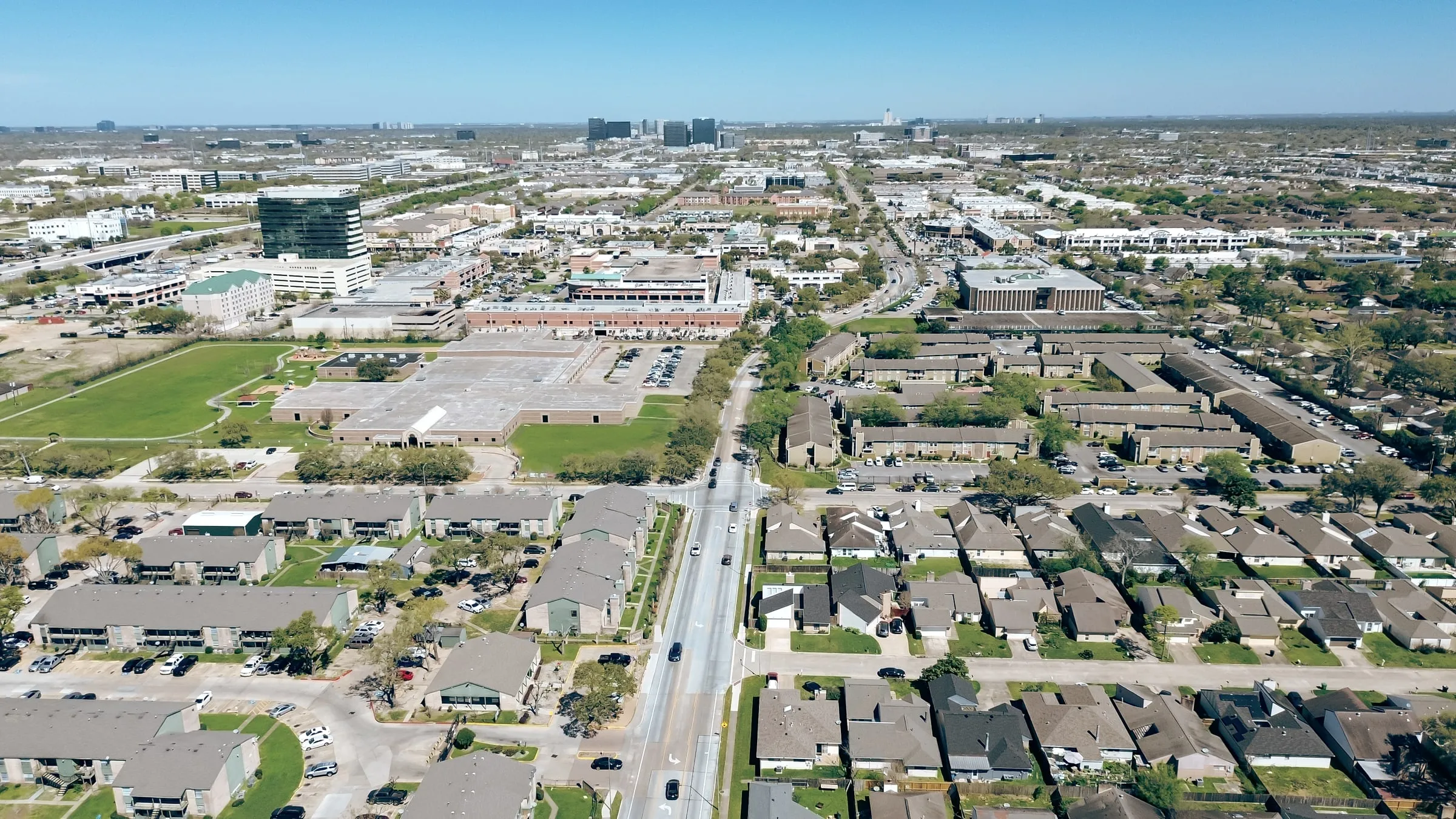 Aerial view of a dense residential neighborhood with office towers in the distance under a hazy sky
