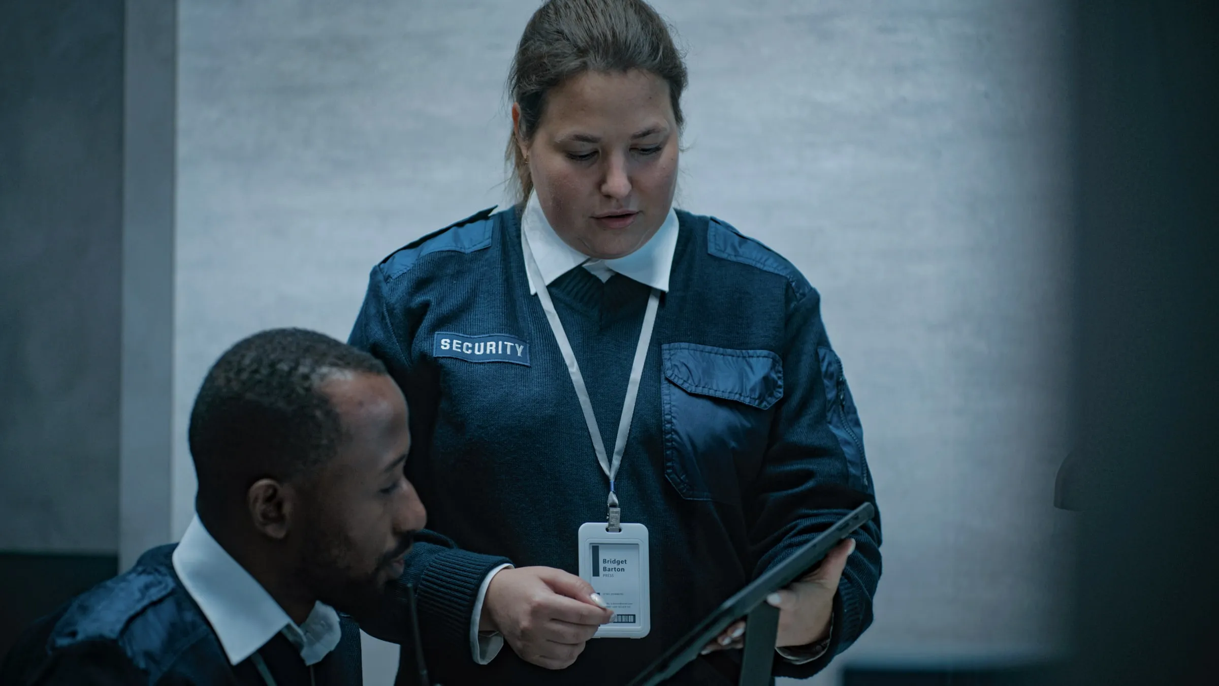 Two security officers in dark uniforms reviewing a tablet together inside a building