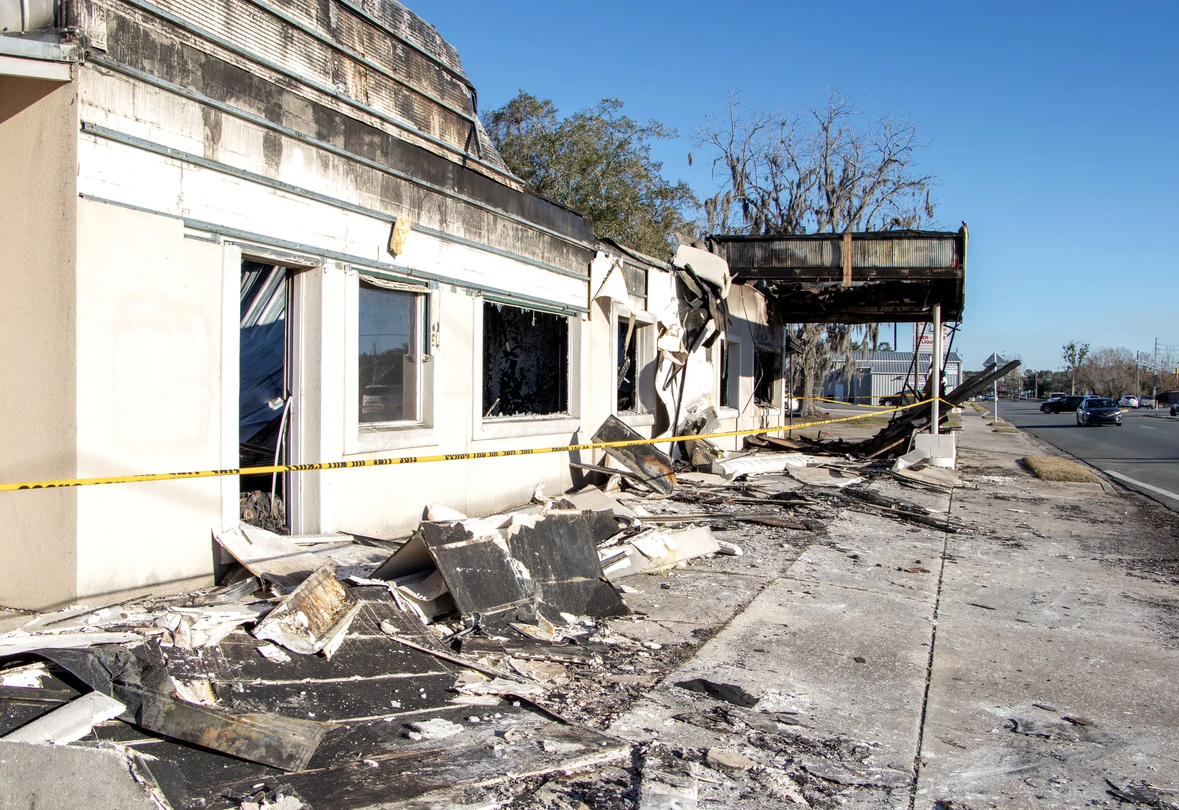 Fire-damaged single-storey commercial building with a collapsed roof, charred debris and yellow caution tape