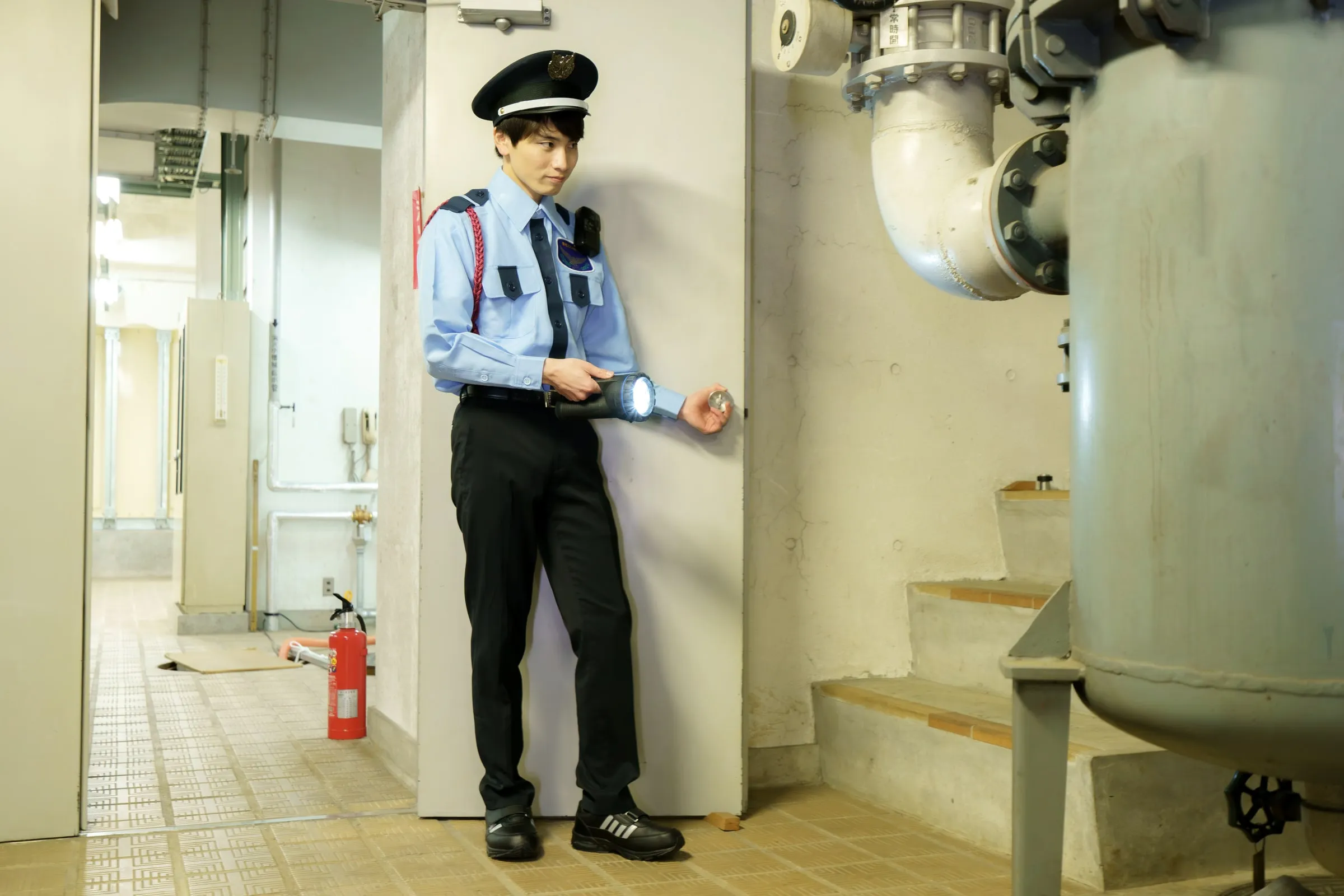 Officer in a light blue uniform and cap standing beside pipework in a basement mechanical room