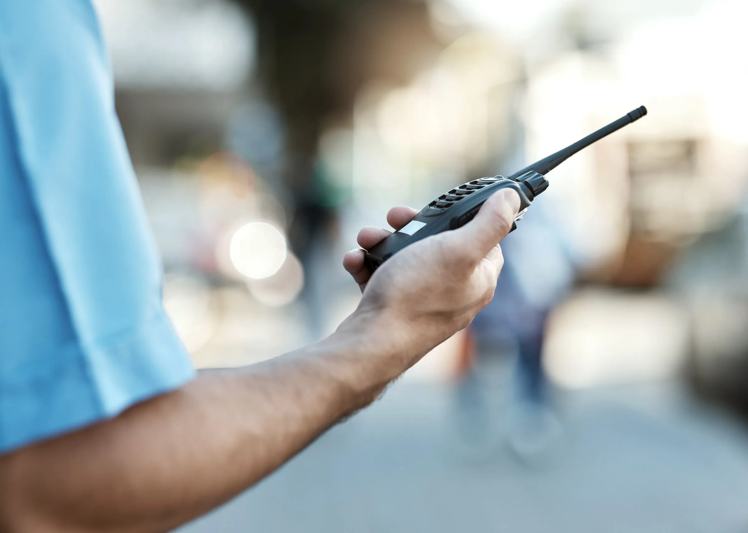 Hand of an officer in a light blue shirt holding a handheld radio in a busy corridor
