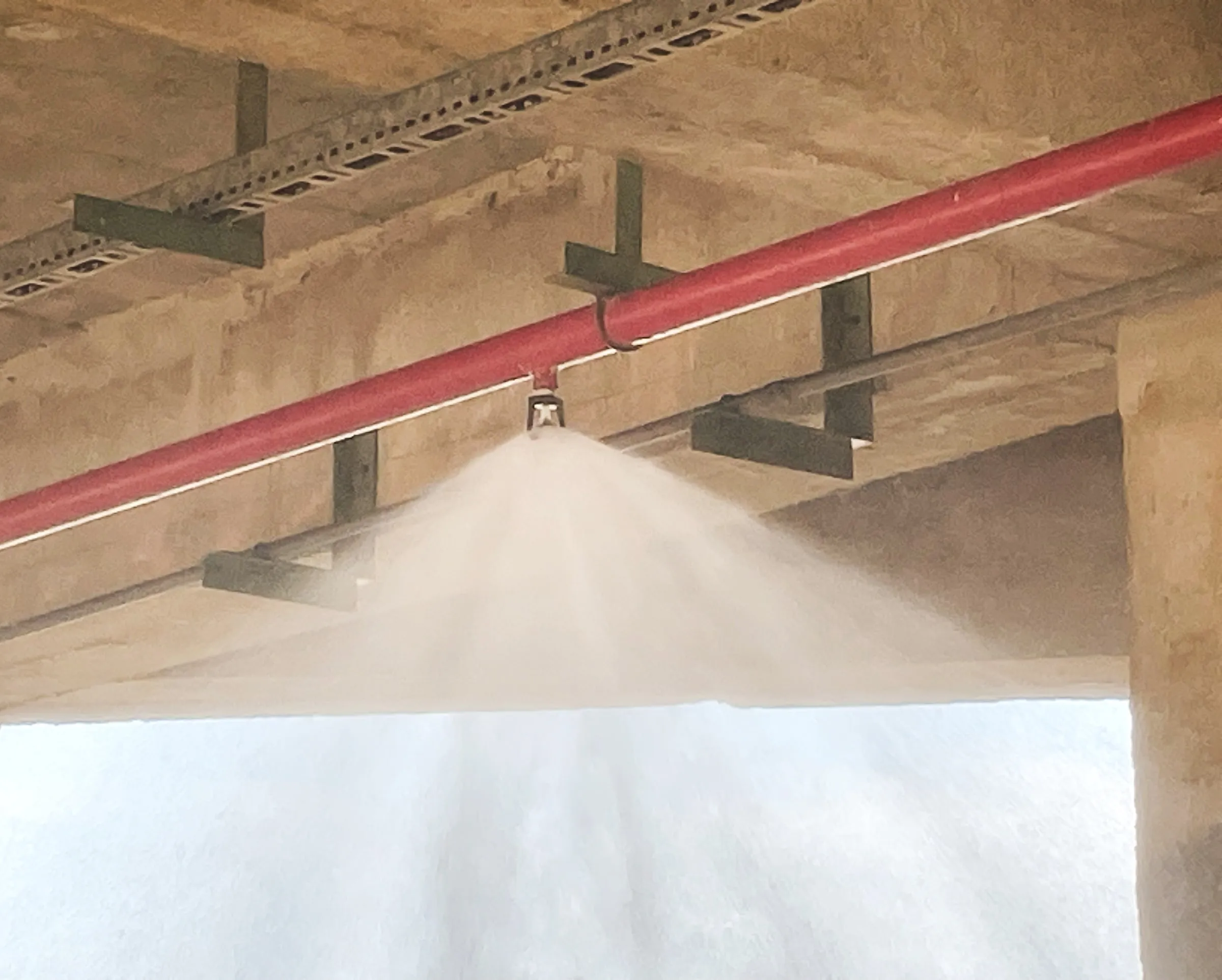 Fire sprinkler head spraying water beneath a wooden ceiling structure