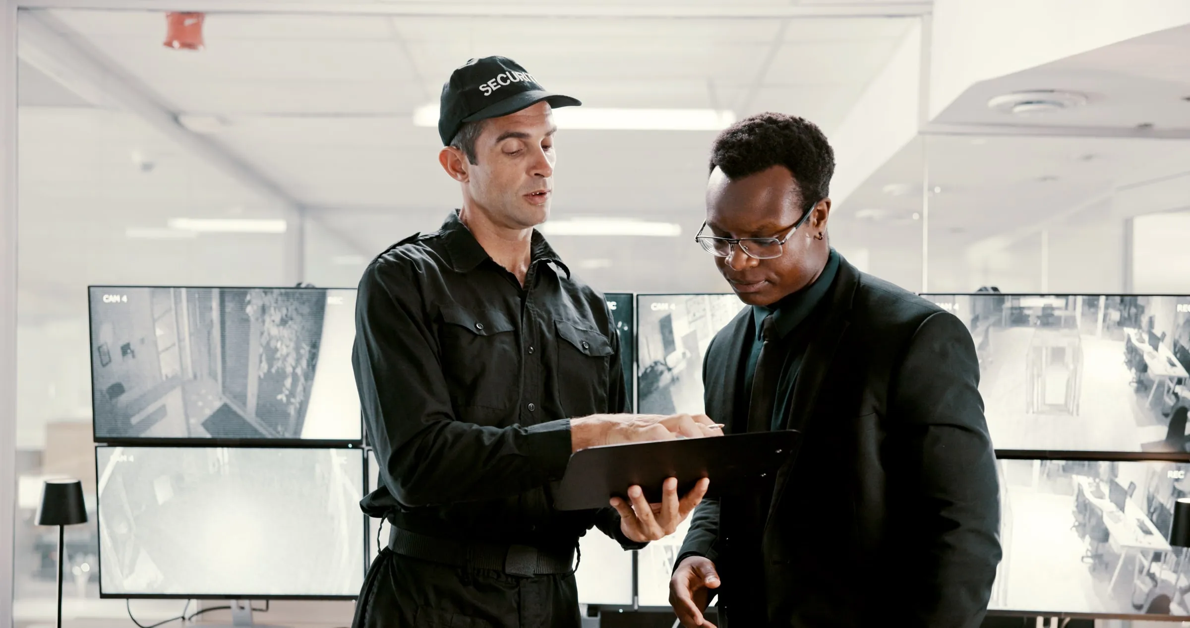 Two security officers in dark uniforms reviewing a clipboard together inside a building